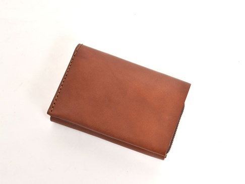 棕色皮革雙折短夾，表面光滑，邊緣有縫線裝飾，右側可見拉鍊。