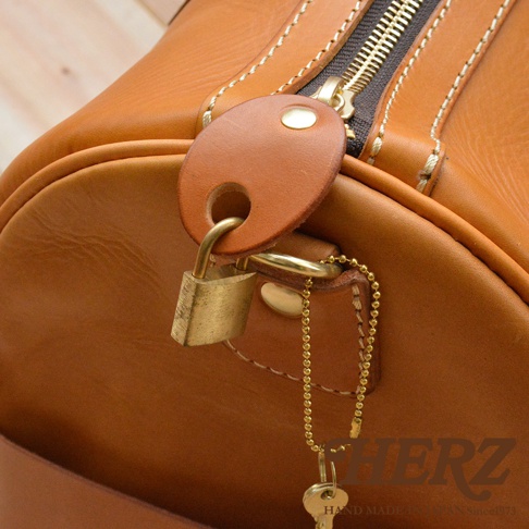 棕褐色皮革波士頓包，配有金色拉鍊、皮革掛牌、鎖頭及鑰匙，鎖頭以金色鍊條連接。