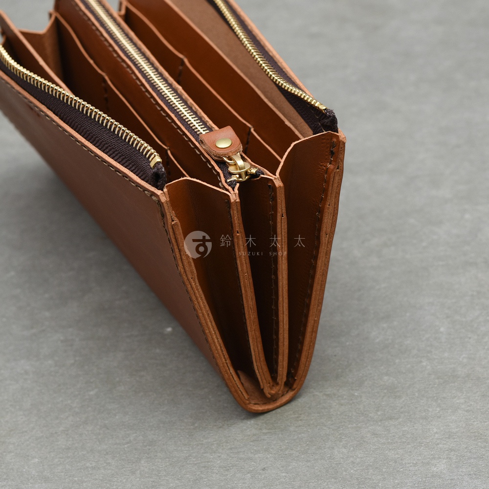 特寫鏡頭展示了棕色皮革拉鍊長夾的側面，內部有三個隔層，展示了其大容量的設計。