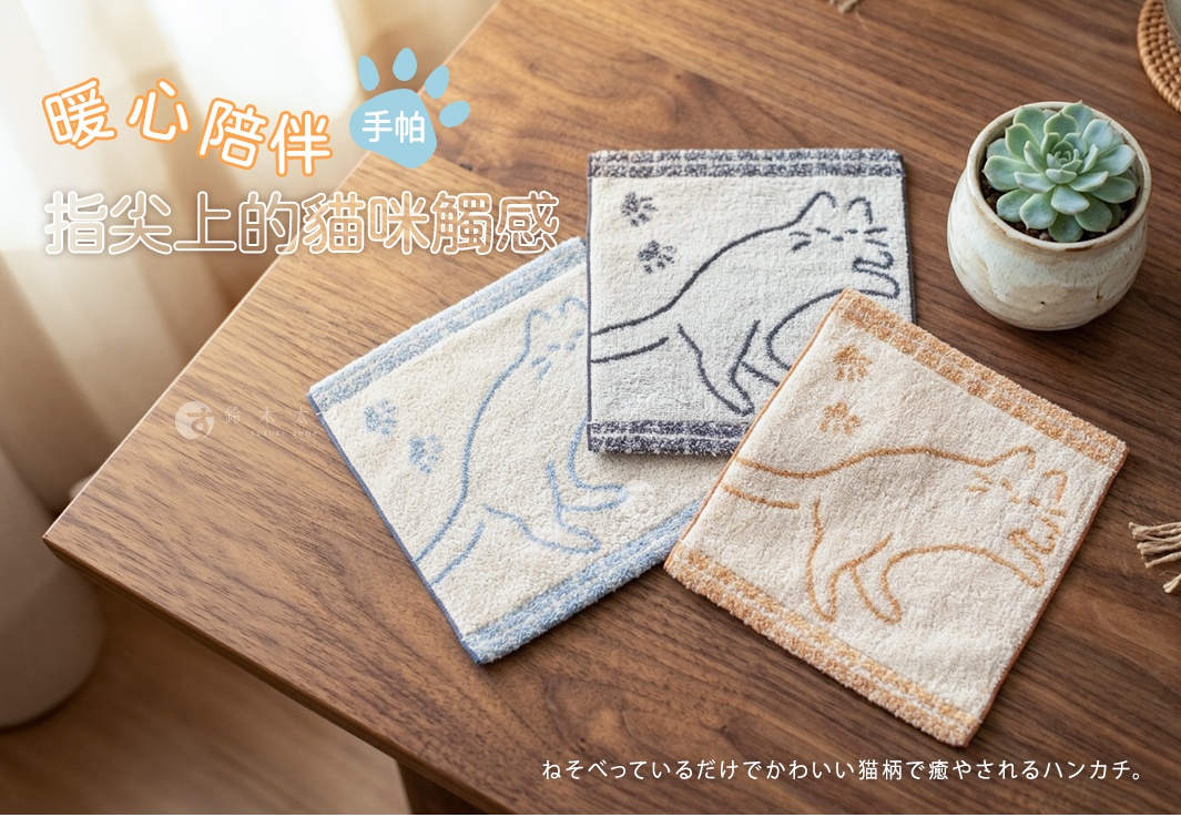 木質桌面上擺放著三條今治午睡貓咪雙色手帕，每條手帕上都有懶洋洋的貓咪剪影與可愛腳印圖案，色調分別為藍、灰、棕，手帕旁還有一盆小型多肉植物裝飾。