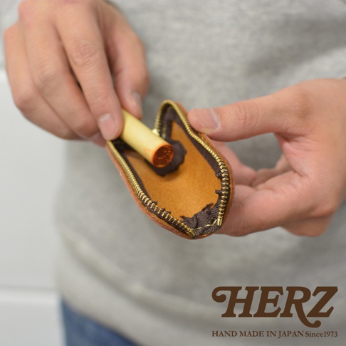 職人手作皮革印章收納袋 KZ-121，採用棕色皮革製作，內襯為淺棕色皮革，搭配金色拉鍊，袋口露出一個木質握柄的印章。