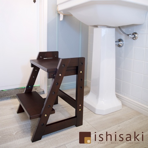 深棕色木藝二階墊腳凳，結構穩固，設有兩層踏板，適合浴室使用，旁邊為白色柱狀洗手盆。