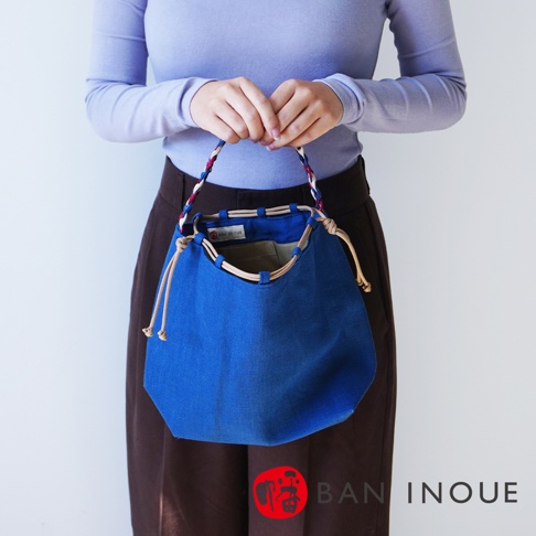 BAN INOUE 麻花辮束口手提包，由一位女士持握，包款為藍色，束口設計，搭配編織提把。