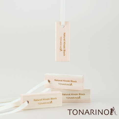 數塊淺色木質檜木條，上面印有「Natural Hinoki Block TONARINO」字樣，其中一塊檜木條懸掛在白色緞帶上，另兩塊堆疊擺放，其中一塊有白色緞帶穿過。