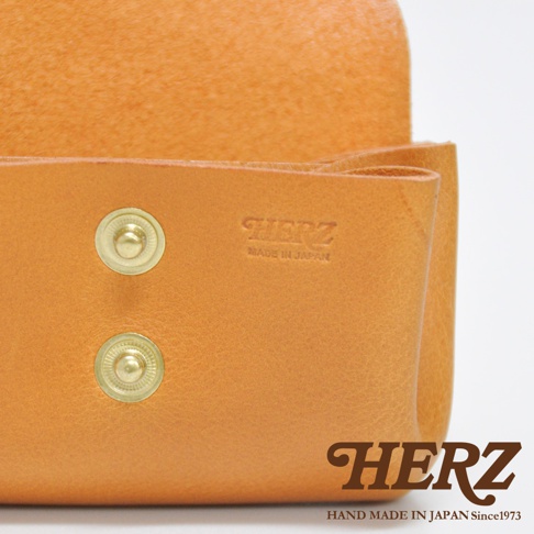 橘棕色皮革三層零錢包，設有兩個金色按扣，皮革表面壓印有「HERZ」品牌標誌及「MADE IN JAPAN」字樣。