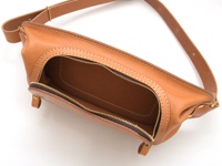 棕色皮革製成的斜背包，主拉鍊開口，展示內部，附有可調節的皮革肩帶。