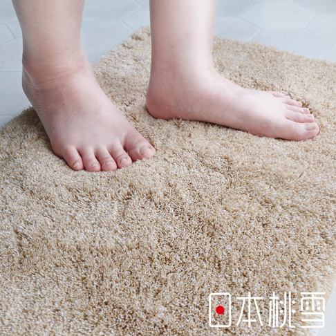 日本桃雪抗菌防臭瞬吸乾爽浴墊，特寫腳踩在柔軟的米色長絨毛浴墊上，展現其舒適的觸感。