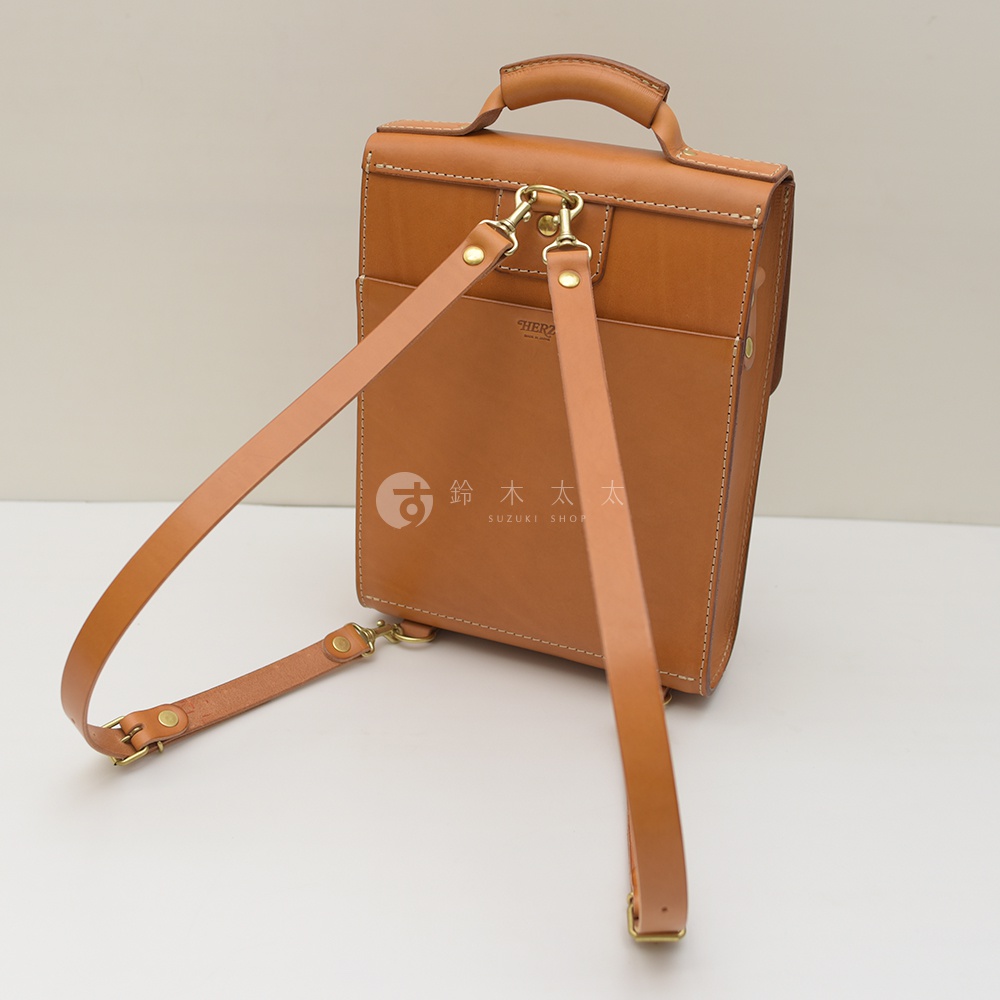 職人手作皮革復古後背包，棕褐色，展示包包背面，帶有可調節肩帶和金色金屬扣環，皮革材質，簡約設計。