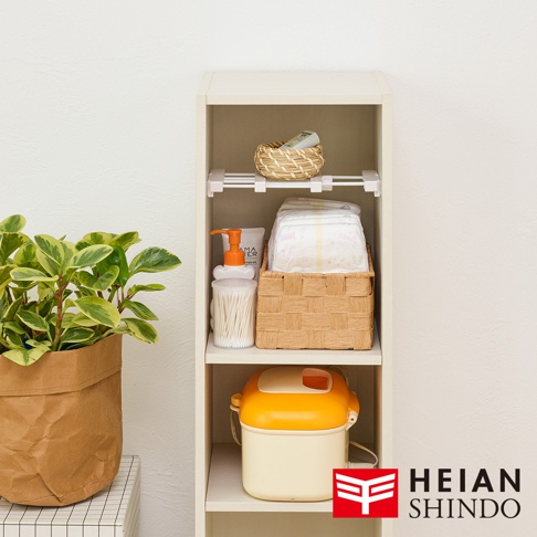以白色為主的收納架，上面擺放著洗衣精、棉花棒、尿布、草編籃及一個黃色蓋子的收納盒，架子旁有一盆綠色植物，右下角有平安伸銅的 Logo。