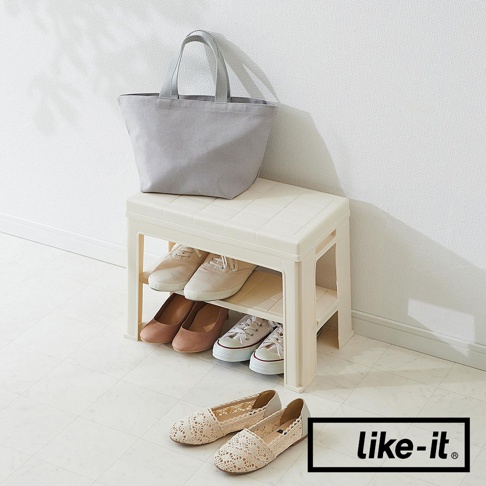 米白色塑膠材質的玄關穿鞋收納椅，上方擺放一個灰色帆布托特包，收納椅下方兩層展示有四雙鞋子，包括兩雙帆布鞋和兩雙高跟鞋。