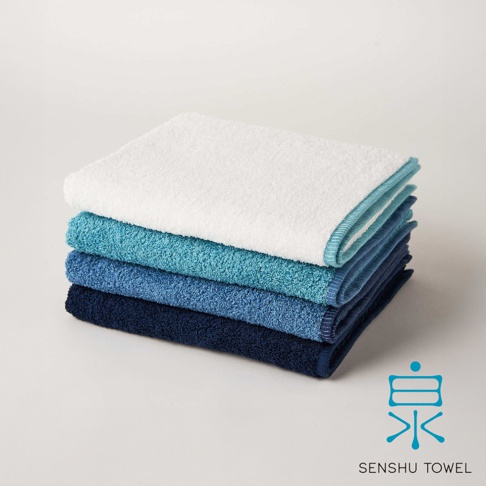 一疊四條 SOLID 細柔蓬韌緞澤長纖毛巾，顏色由上至下分別為白色、淺藍、藍色及深藍。毛巾材質看起來柔軟，邊緣有滾邊設計。