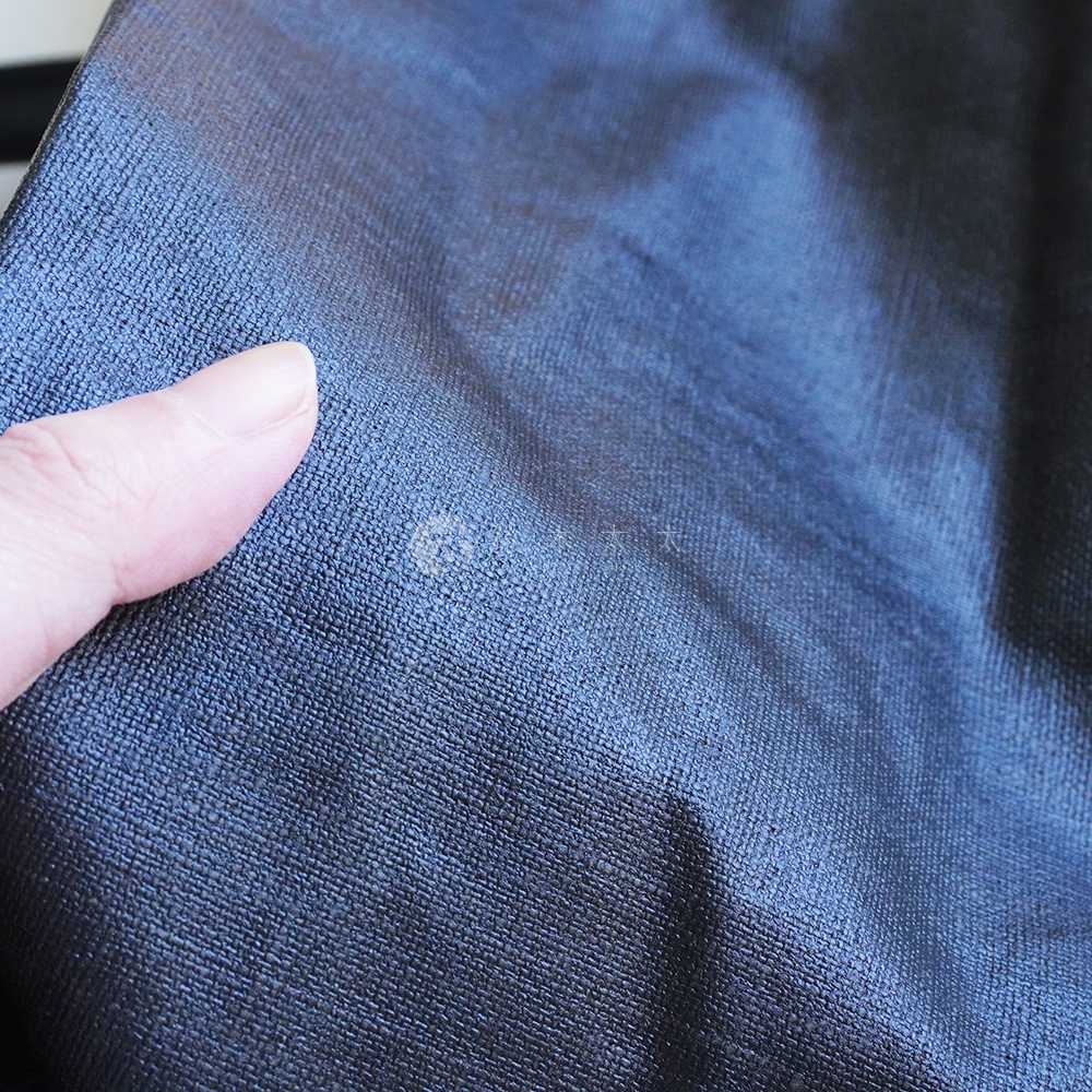 深藍色亞麻布料上有一個淺色污漬，一根手指在左側輕輕觸碰布料。