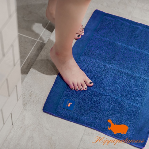 深藍色竹棉浴墊，表面柔軟，帶有條紋紋理，左下角有橘色小標籤，右下角印有橘色河馬圖案和品牌名稱。