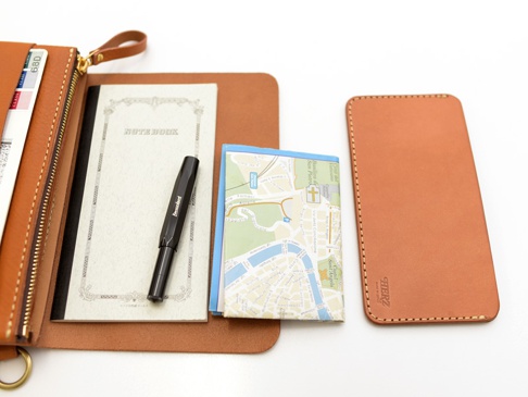 職人手作皮革旅行護照收納長夾，呈現自然的淺棕色皮革，內部包含一本筆記本、一支黑色鋼筆及一張摺疊地圖。