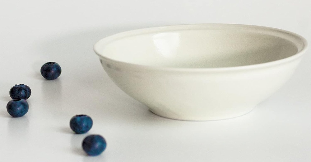 Ciel 美濃燒簡約素雅釉彩淺碗，呈米白色，陶瓷材質，碗身線條圓潤，內側光滑，外側帶有細膩的釉彩紋理。旁有幾顆藍莓點綴。