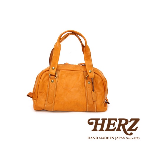 職人手作皮革水洗加工迷你波士頓包，呈現溫暖的橘黃色調。包款採用柔軟的皮革材質，透過水洗加工處理，呈現獨特紋理與自然皺褶感。設有雙提把與簡潔的包身設計，散發復古質感。