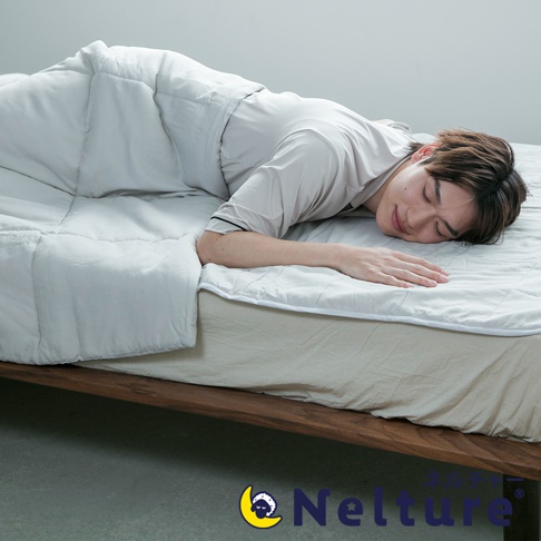 淺灰色五層散熱涼感單人被，鋪在木製床架上，一名男子側臥於被中，臉部朝下，閉眼休息。被子表面有菱格紋縫線。