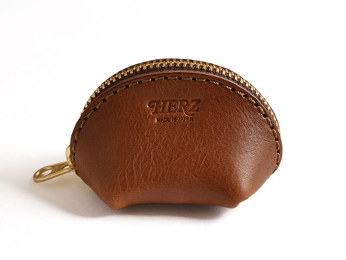 職人手作的棕色皮革貝殼造型零錢包，配有黃銅拉鍊和品牌烙印。