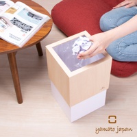 淺木紋色與白色搭配的方形積木垃圾桶，內部有透明塑膠袋，一只手正將揉成團的紙張丟入。