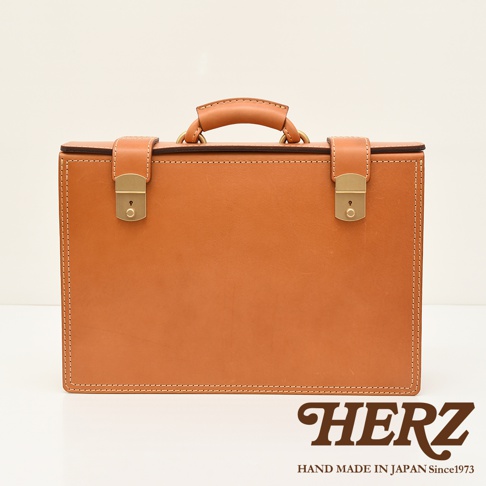 職人手作皮革機師箱，採用天然皮革製成，箱體為淺棕色，配有金色鎖扣和提把，車縫線明顯，風格復古。