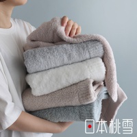 一位女子手捧著一疊顏色柔和的毛巾，上面印有「日本桃雪」的標誌。