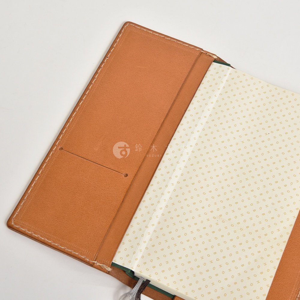 皮革旅行記事本書套，帶有兩個內插槽，顏色為淺棕色，配有白色縫線。內頁為淺米色，印有重複的金色圓形圖案。