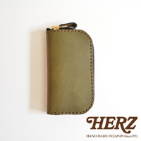 橄欖綠皮革橢圓形鑰匙包，拉鍊開合，手工縫線，品牌HERZ標誌。