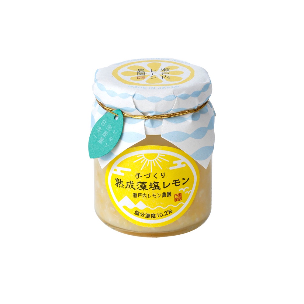 玻璃罐裝有熟成的藻鹽漬檸檬，內容物呈現淡黃色。罐子上方覆蓋著印有藍色海浪圖案的白色紙蓋，並以金色繩索固定。一塊淺綠色的標籤掛在繩索上，上面寫著日文。罐身貼著一個黃色橢圓形標籤，中央有太陽圖案，下方標示著產品名稱「熟成藻鹽漬檸檬」及其他日文資訊。