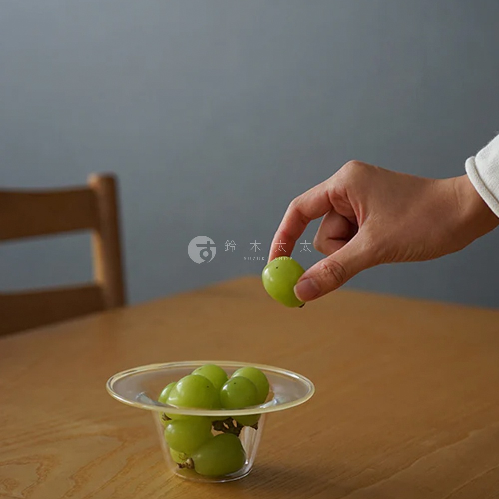 一只手拿起一顆綠色葡萄，旁邊是裝有綠色葡萄的透明玻璃深型點心碗，碗邊緣有擴展設計。