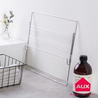 金屬網格折疊式晾曬架，帶有多層晾衣桿，可懸掛衣物。旁邊有一個黑色網籃，裡面裝有疊好的白色毛巾，以及一瓶深棕色液體的瓶子。