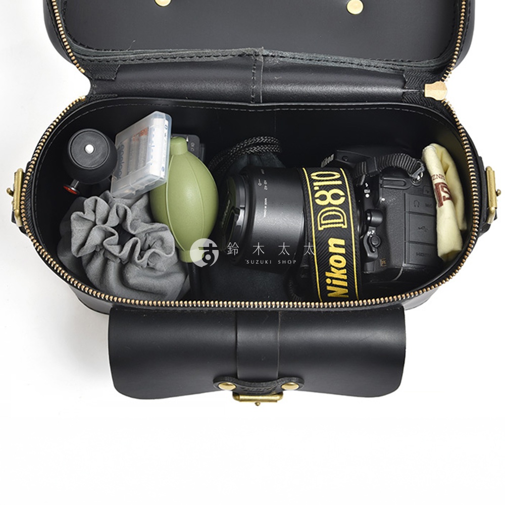 一個黑色皮革相機包，裡面裝有相機、鏡頭、電池、吹塵球和一塊布，包包上有 Nikon D810 的字樣。