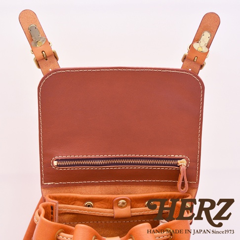 職人手作皮革復古風旅行後背包，展示棕色皮革材質、金屬釦環和拉鍊細節，以及抽繩開口設計。