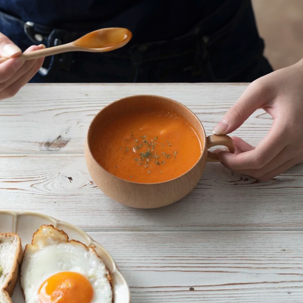 楓木製湯杯碗，呈圓形，帶有彎曲的把手，碗內盛有橘紅色湯品，表面撒有綠色香料。