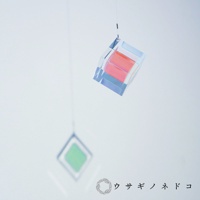 透明稜鏡立方體吊飾，內部有粉紅色層次，透過光線折射呈現藍紫色光澤。下方懸掛著一個綠色菱形吊飾。