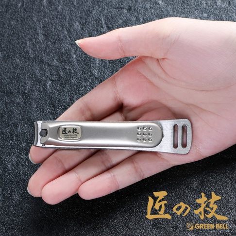 手握銀色不鏽鋼曲刃指甲剪，上面有日文「匠の技」和英文「High Quality Nail clipper」標誌，以及9個小圓點和兩個長方形孔的防滑設計。