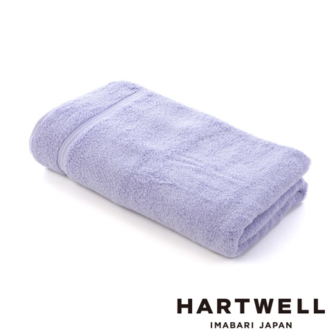 一條淡紫色、輕盈柔軟的浴巾，材質為純棉，表面有細緻絨毛，邊緣有條紋裝飾，折疊後呈長方形，背景為純白色。