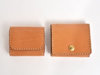 兩個棕褐色皮革製的雙折收納零錢包，其中較大的零錢包有一個金色圓形按扣。兩個零錢包均以白色縫線手工製作，邊緣圓潤。