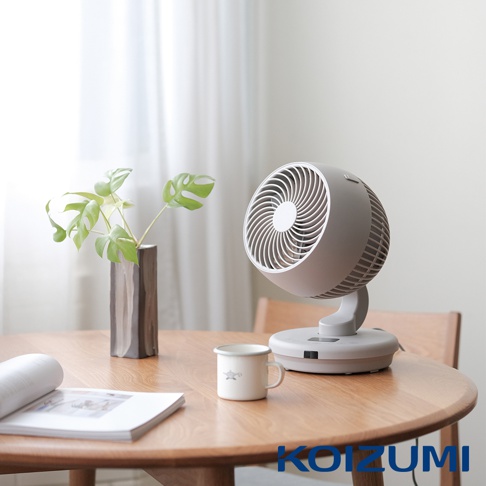 灰色鵝頸式循環扇，帶有圓形風扇網罩和可調節的底座，擺放在木製圓桌上，旁邊有植物裝飾的陶罐和一個帶有圖案的白色馬克杯。