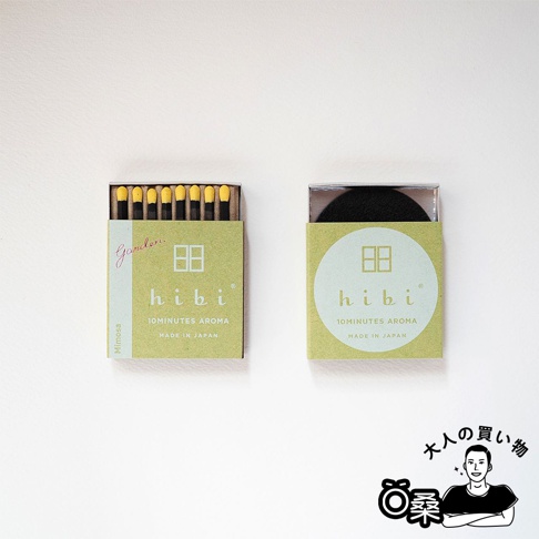 一盒綠色紙盒裝有黑色火柴桿及黃色火柴頭的香氛火柴，另一盒綠色紙盒內裝有黑色圓形物體，兩盒皆印有「hibi 10MINUTES AROMA MADE IN JAPAN」字樣。