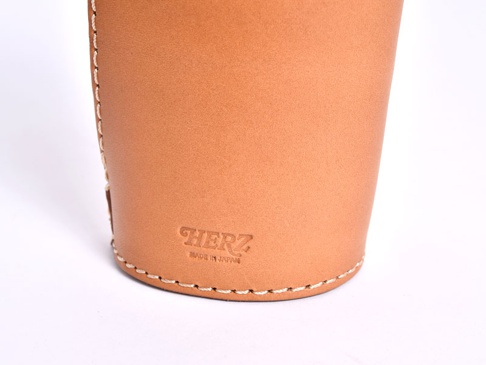 淺棕色皮革製成的直立式筆袋，表面壓印有「HERZ」品牌標誌及「MADE IN JAPAN」字樣，邊緣以白色縫線裝飾。