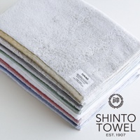 YUKINE 雪中漫步系列有機棉蓬厚浴墊，層疊展示多種柔和色系，包括淺灰、米黃、淺綠、紅色、藍色等。浴墊材質蓬鬆柔軟，邊緣車縫整齊，頂部可見白色標籤，印有品牌名稱及日文。