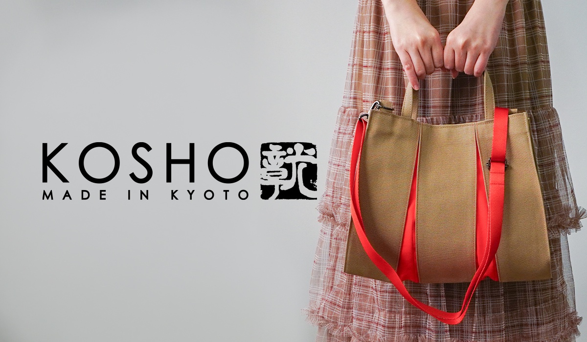 KOSHO MADE IN KYOTO 的品牌標誌旁邊，展示一個棕色帆布托特包，上面有亮紅色的帶子，由一位身穿格子連衣裙的女士手提著。