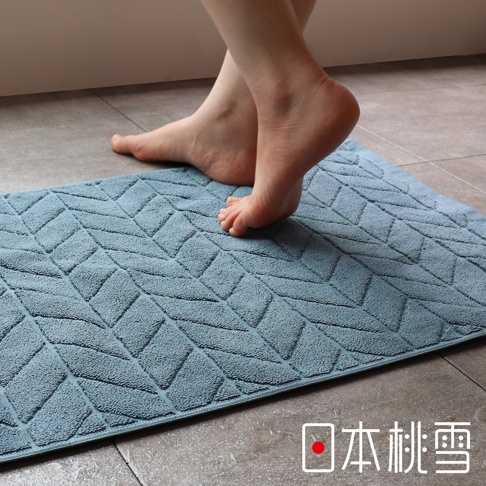 一雙赤腳踩在淺藍色幾何圖案的吸水浴墊上，腳趾微微彎曲，浴墊上的紋路清晰可見。