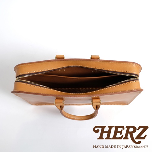 職人手作淺棕色皮革公事包，頂部視角，拉鍊開啟，露出內部隔層，附有兩個提把。