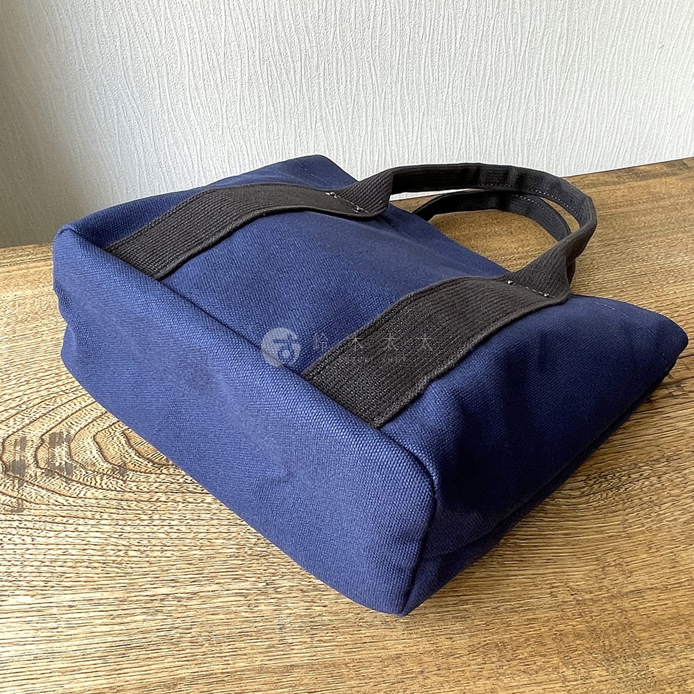 深藍色帆布水桶托特包，配有黑色織帶提把，簡潔的設計。