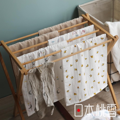一個木製晾衣架上掛著幾條印有可愛圖案（彩虹、月亮、小黃花）的紗布巾，其中兩條深色針織襪子夾在晾衣架上，右下角有「日本桃雪」的紅色圓點標誌