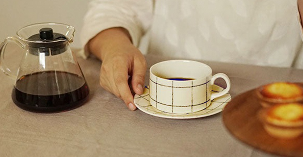 gohara mamiko 美濃燒手繪馬克杯，米白色陶瓷杯身，搭配簡約線條格紋，附同款杯盤，一旁擺放著玻璃咖啡壺與兩份蛋塔。