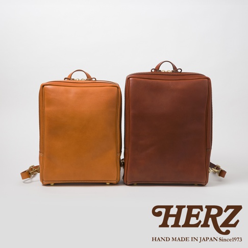 兩個職人手作皮革軟皮商務後背包，一個為淺棕色，另一個為深棕色。兩款背包皆為方形簡約設計，採用光滑皮革材質，並配有頂部提把及肩帶。