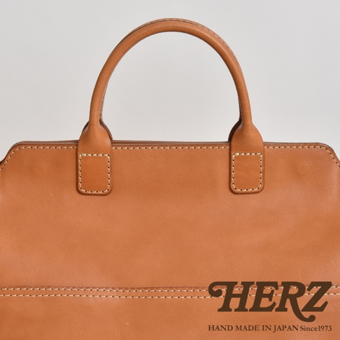 職人手作皮革大容量兩用托特包，展示為棕褐色，全皮革材質，搭配米白色縫線。包款設計簡潔，擁有圓弧形提把，適合日常攜帶。