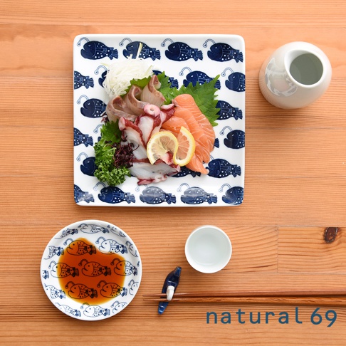 cocomarine × Janke 方形餐盤，白色陶瓷盤面印有藍色卡通魚圖案，盤中盛放著生魚片、章魚、檸檬片與芝麻葉。